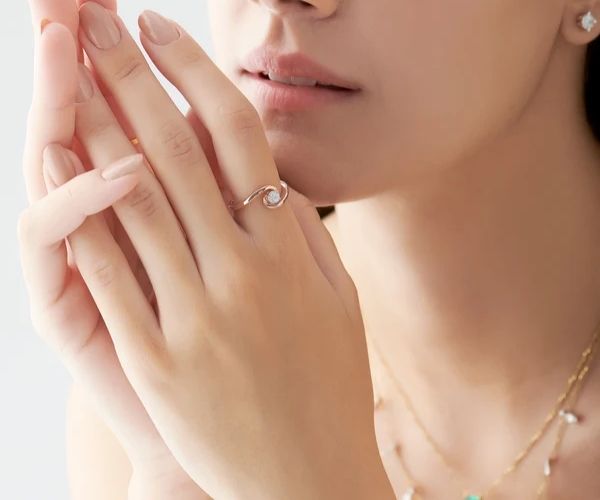 Close-up of a hand wearing a ring with a pearl on a light background