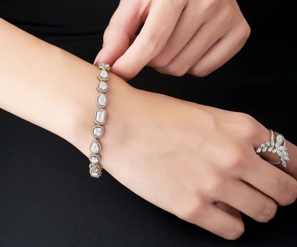 Hand wearing a diamond bracelet and ring on a black background