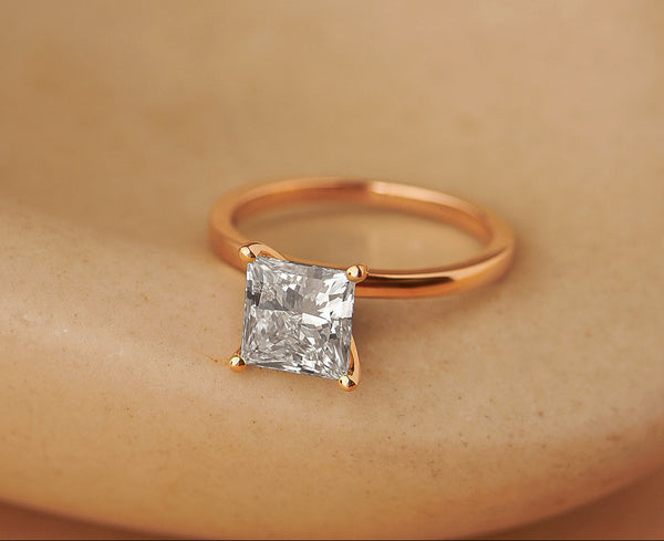 Rose gold ring with a square-cut diamond on a beige background