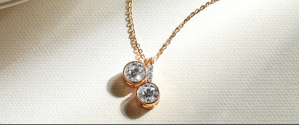 Rose gold necklace with two round gemstones on a light beige background