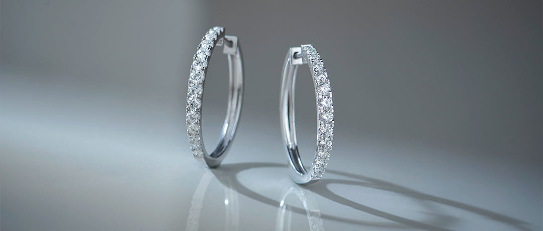 Pair of silver hoop earrings on a reflective surface with a gray background