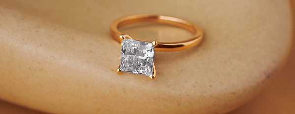 Gold ring with a square-cut diamond on a beige background