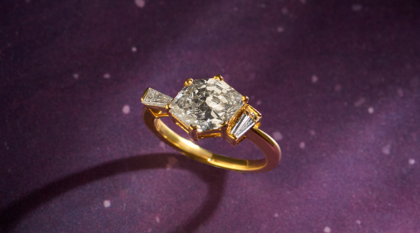 Gold ring with a large central diamond and smaller side diamonds on a purple background Gold ring with a large central diamond and smaller side diamonds on a purple background