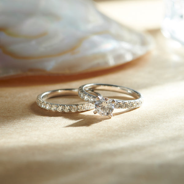 Two diamond rings on a soft, beige surface with a blurred shell in the background.