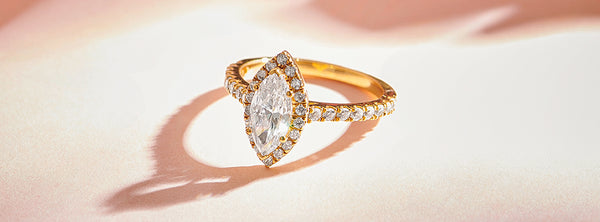 Gold ring with a large central diamond and smaller diamonds on a soft pink background