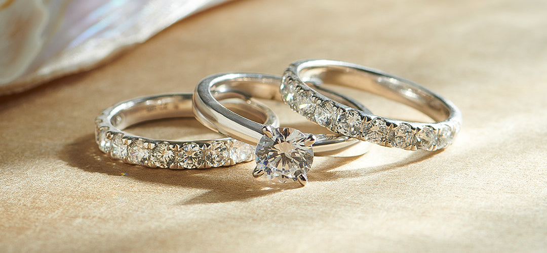 Three silver rings with diamond accents on a beige surface