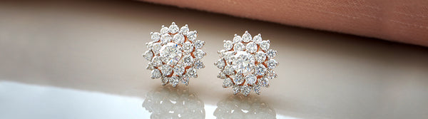 Pair of diamond earrings on a reflective surface with a neutral background