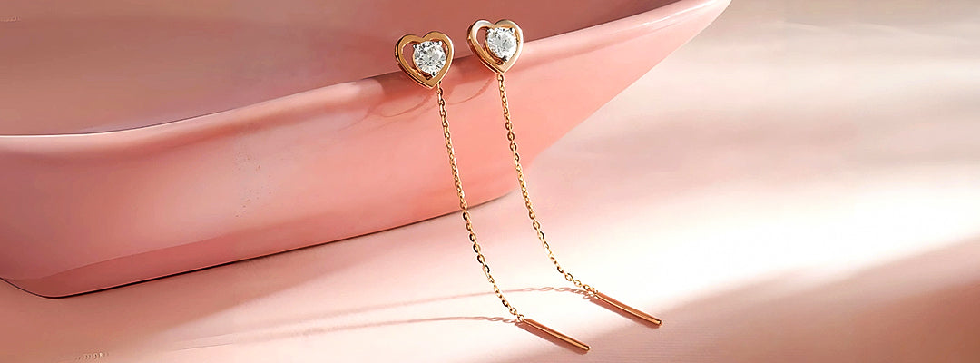 Heart-shaped earrings with dangling elements on a pink fabric background