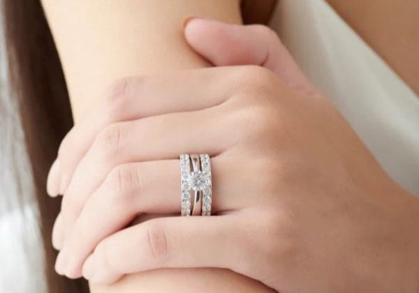 Close-up of a hand wearing two diamond rings on a neutral background