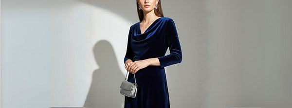 Woman wearing a blue velvet dress holding a small handbag against a plain background
