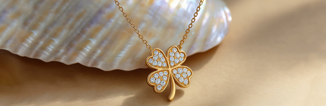 Gold four-leaf clover necklace with diamond accents on a beige background