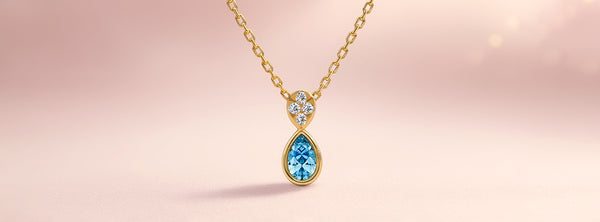 Gold necklace with a teardrop-shaped gemstone pendant on a pink background