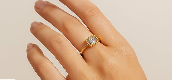Gold ring with a diamond on a hand against a beige background