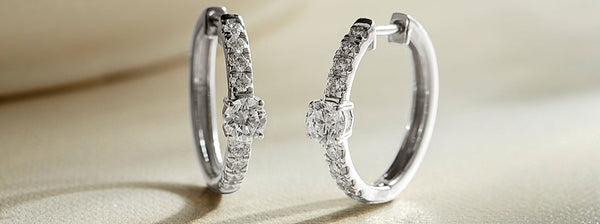Pair of white gold hoop earrings with embedded diamonds on a light background
