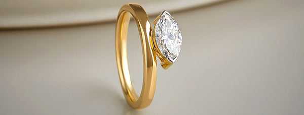 Gold ring with a pear-shaped diamond on a beige background