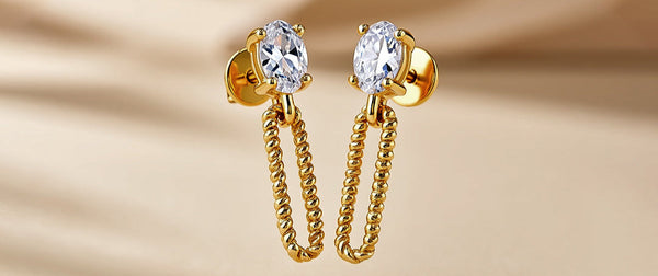 Gold earrings with clear gemstones on a beige background
