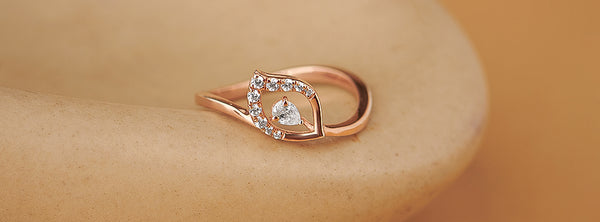 Rose gold ring with heart design and embedded diamonds on a beige stone surface