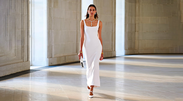 Woman in a white dress walking in a large, open hall with high ceilings.