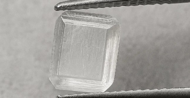 Raw diamond held by tweezers on a gray background